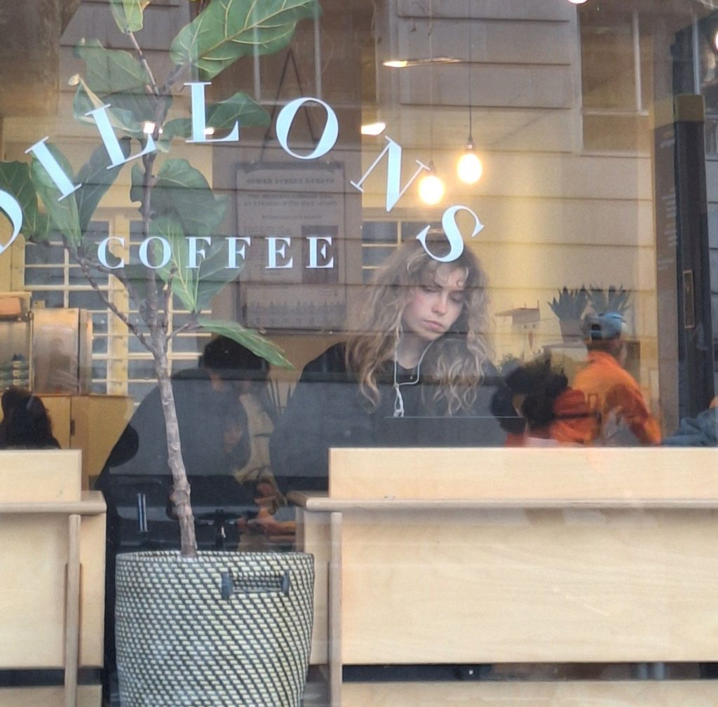 A person working through a W:2 course on a laptop at a coffee shop window
